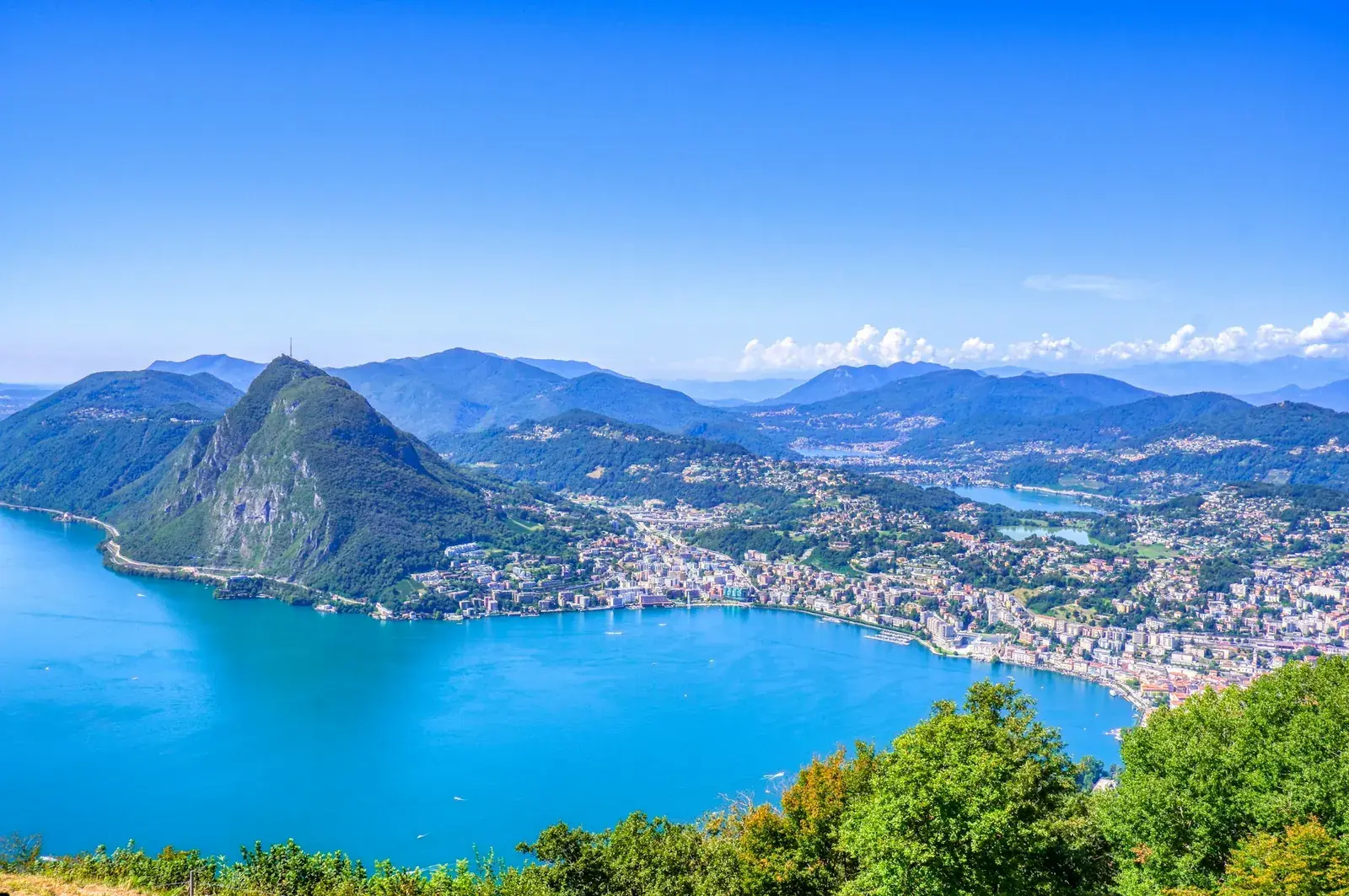 Vista dall'alto di Lugano: il lago azzurro, il Monte San Salvatore e la città lungo la riva.